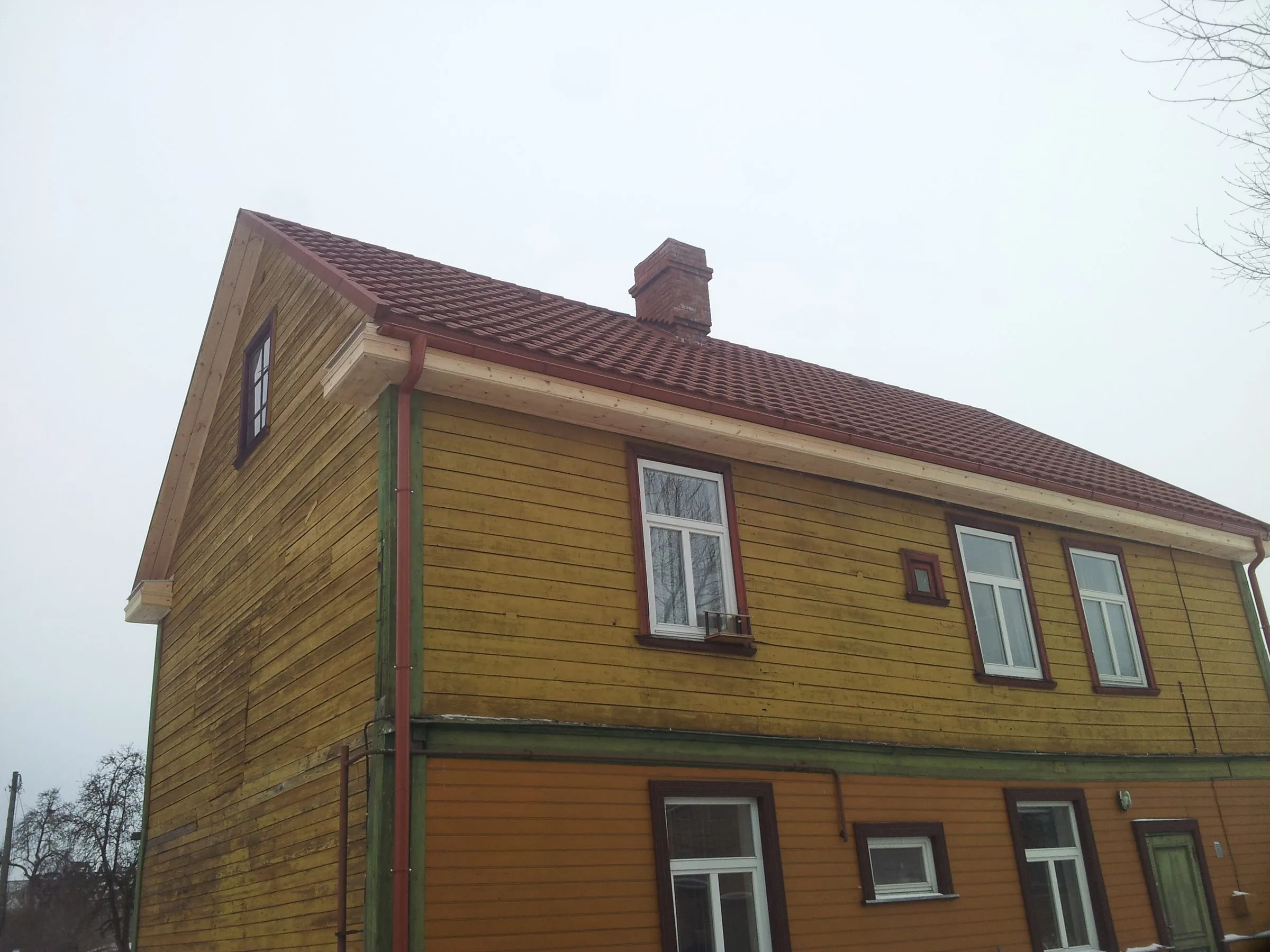 Koka māja ar sarkanbrūnu metāldakstiņu jumtu