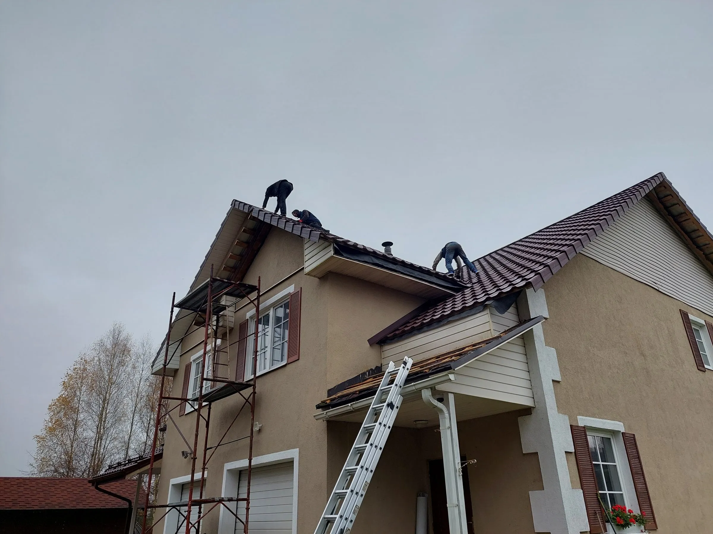 Jumiķi ieklāj brūnu metāldakstiņu jumtu divstāvu mājai